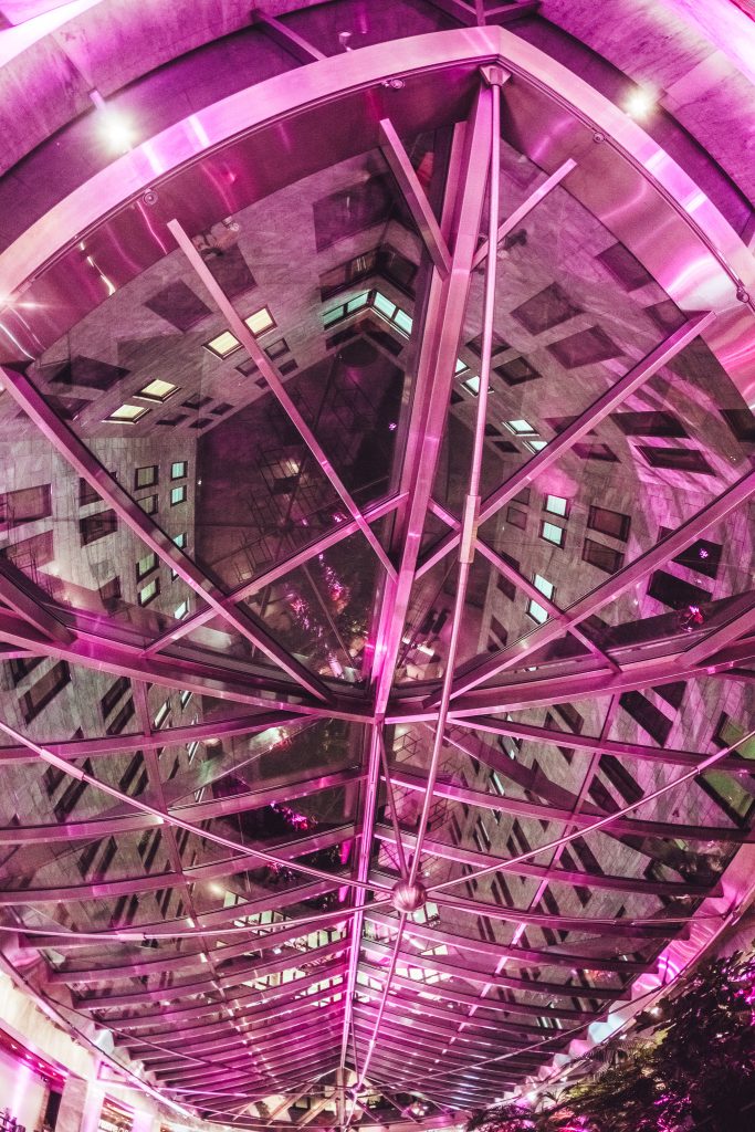 Geometric glass dome interior with pink lighting and intersecting steel beams in an atrium.