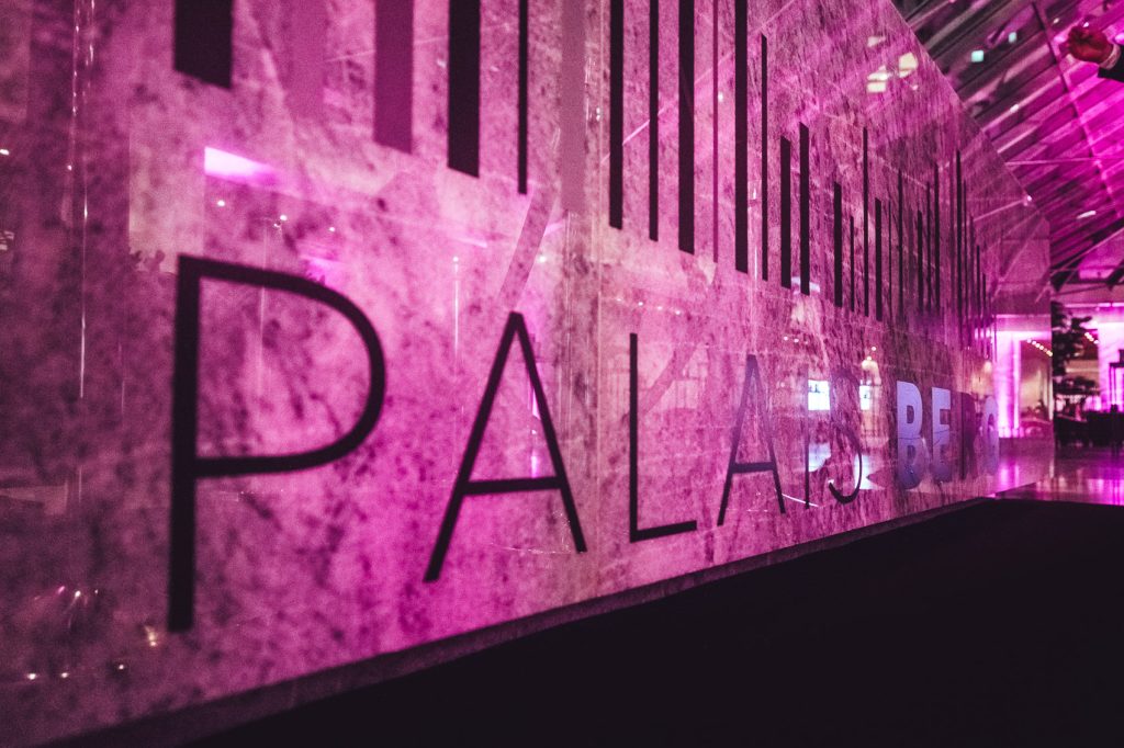 Industrial-style gallery wall with large black letters bathed in pink lighting as part of an exhibit.