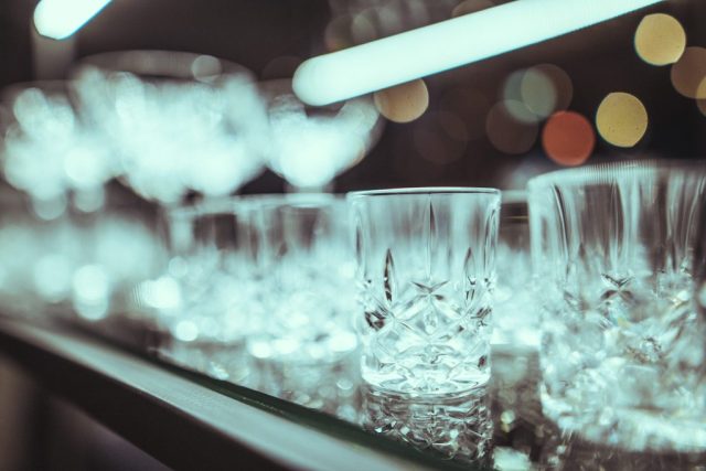 Close-up of a crystal glass on a bar counter with blurred city lights in the background.