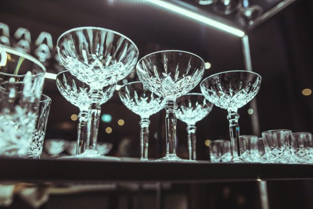 Crystal stemware arranged on a bar shelf with warm lighting and reflections on the glass surfaces.