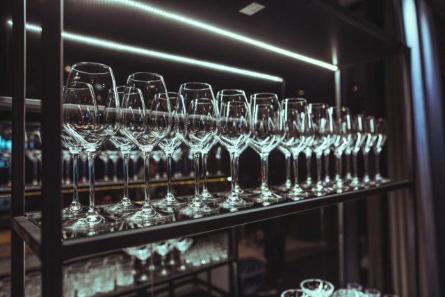 Row of tall wine glasses on a backlit bar display surface.