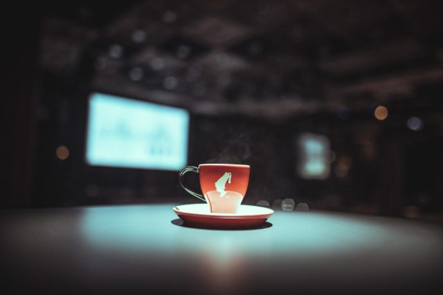 Red coffee cup on a matching saucer with steam rising, set on a dark table and a blurred bokeh background
