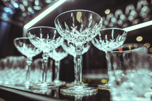 Close-up of a crystal champagne coupe on a bar, with blurred blue bokeh lights in the background.