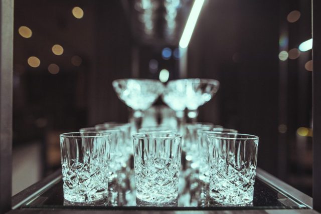 Row of cut-crystal glasses lined up on a reflective bar surface with soft circular bokeh lights in the background