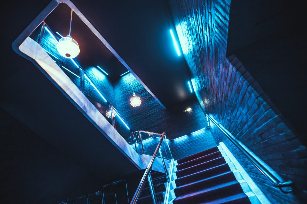 Blue-lit modern staircase with brick walls and hanging lanterns in a dark interior. (Informative architectural photo)